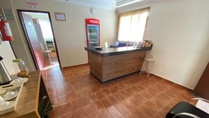 A reception area with a Coca-Cola refrigerator, a wooden reception desk, a bar area, and a seating area with chairs. - Hotel Londe (Patrocinio)