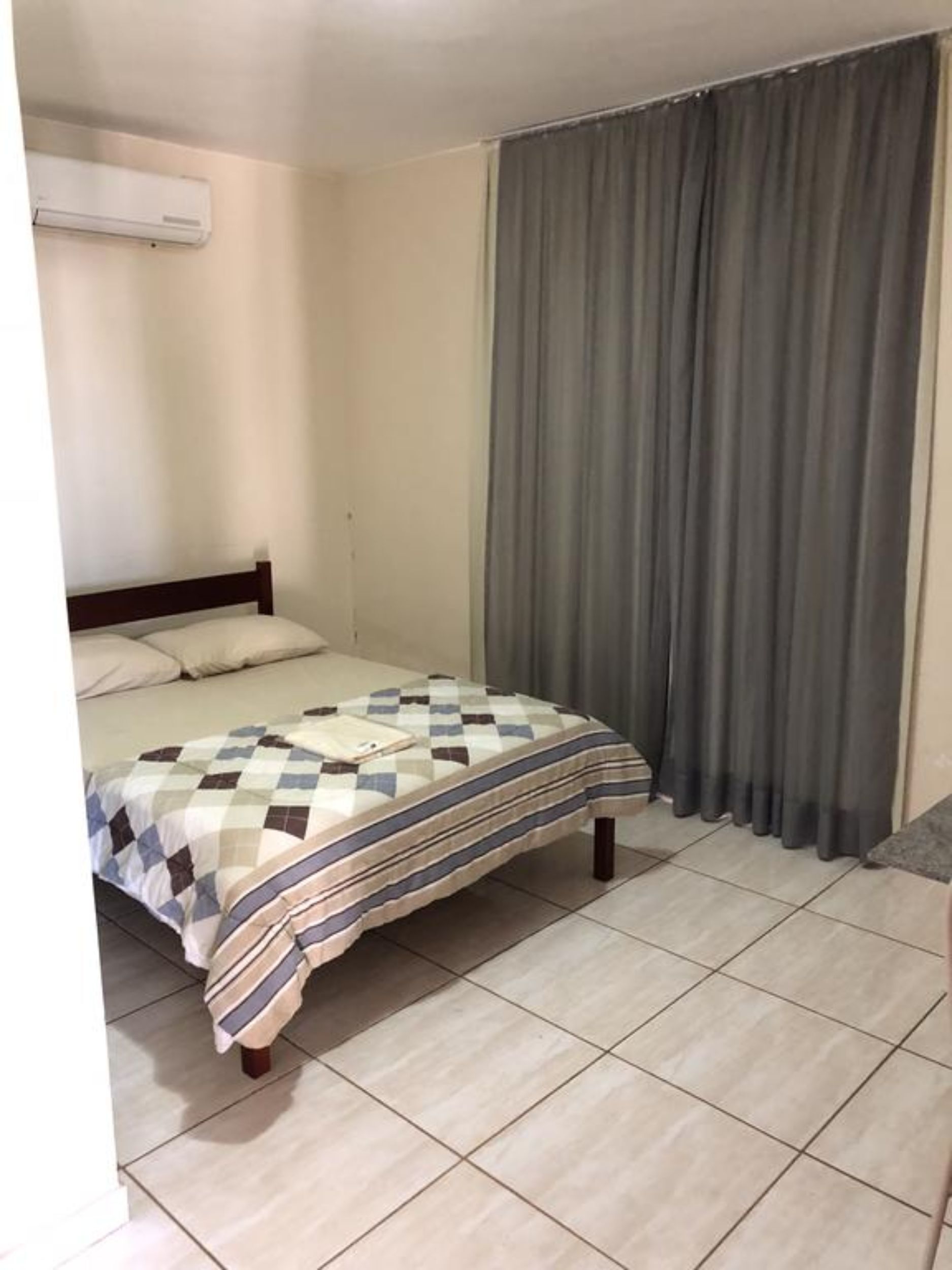 A single bed with a checkered bedspread, a headboard, and a wall-mounted air conditioner.