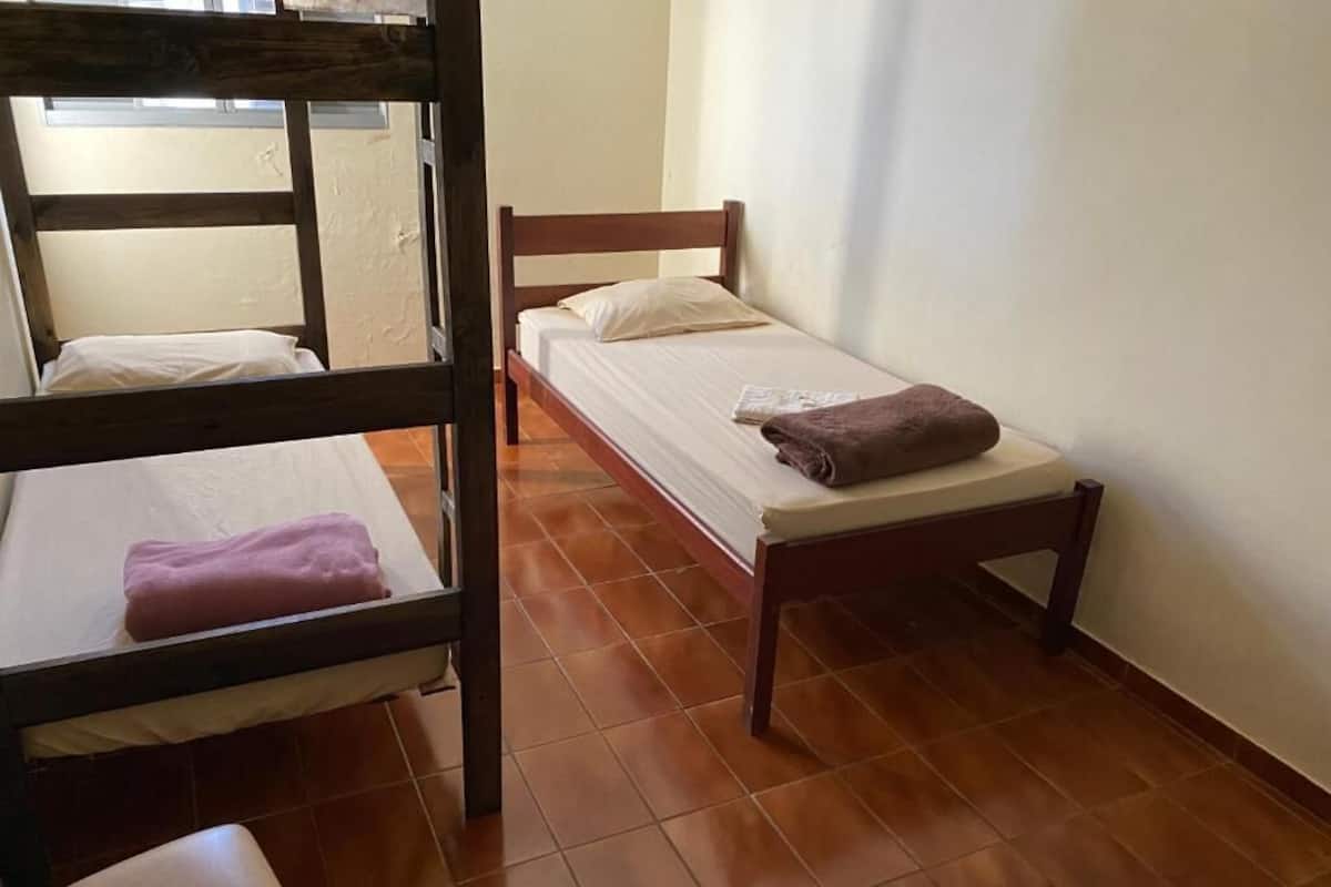 A dormitory room with two bunk beds, a small table, and a window providing natural light.