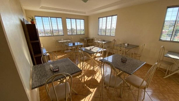 A spacious dining area with multiple tables and chairs, large windows offering a view, and a tiled floor. - Hotel Londe (Patrocinio)