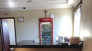 A reception area with a Coca-Cola refrigerator, a wooden counter, and a single stool. - Hotel Londe (Patrocinio)