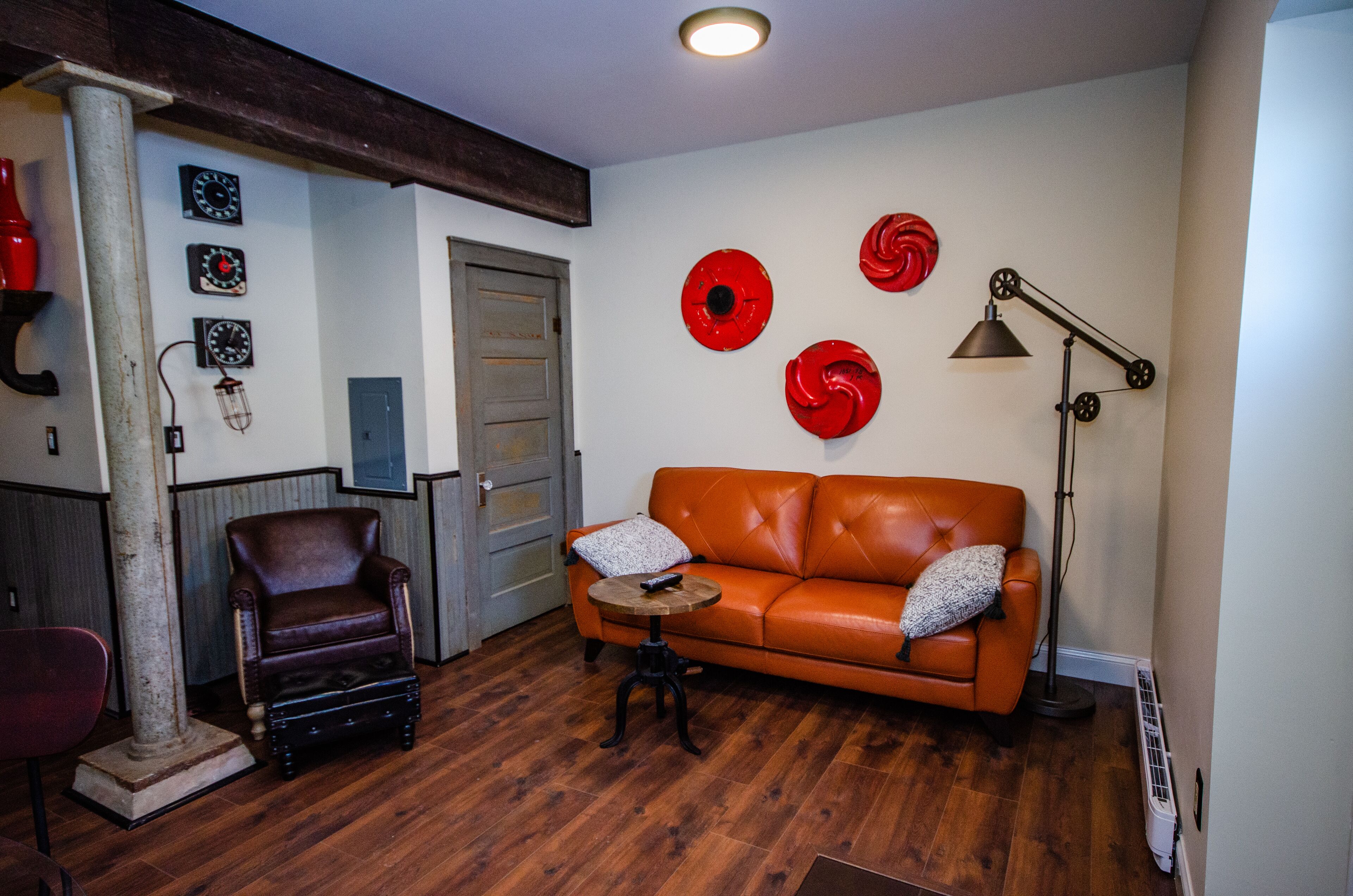 Un salon avec un canapé en cuir marron, une table basse en bois, un fauteuil en cuir marron et un lampadaire rouge.