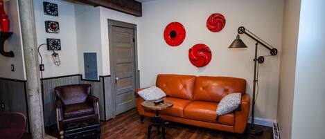 A living room with a brown leather sofa, a wooden coffee table, a brown leather armchair, and a red floor lamp.