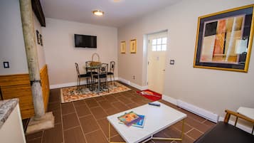 A room with a dining table, chairs, a TV mounted on the wall, and a framed artwork.