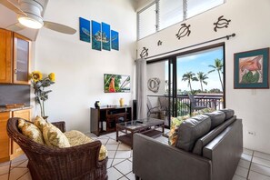 A spacious living area with a large window, a dining table, and a sofa. There are wall art pieces and a decorative plant. - Kona Alii 512: Tropical Oceanview Condo w/ Shared Pool in Downtown Kona (Kailua Kona)