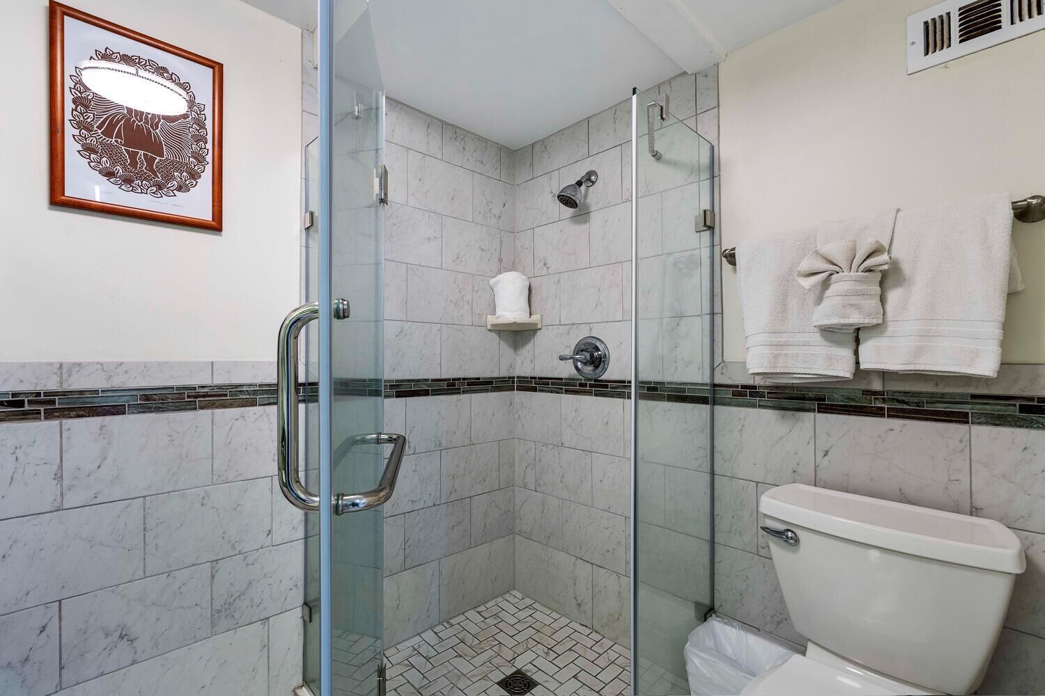 A modern bathroom with a glass shower enclosure, a toilet, and a framed artwork on the wall.