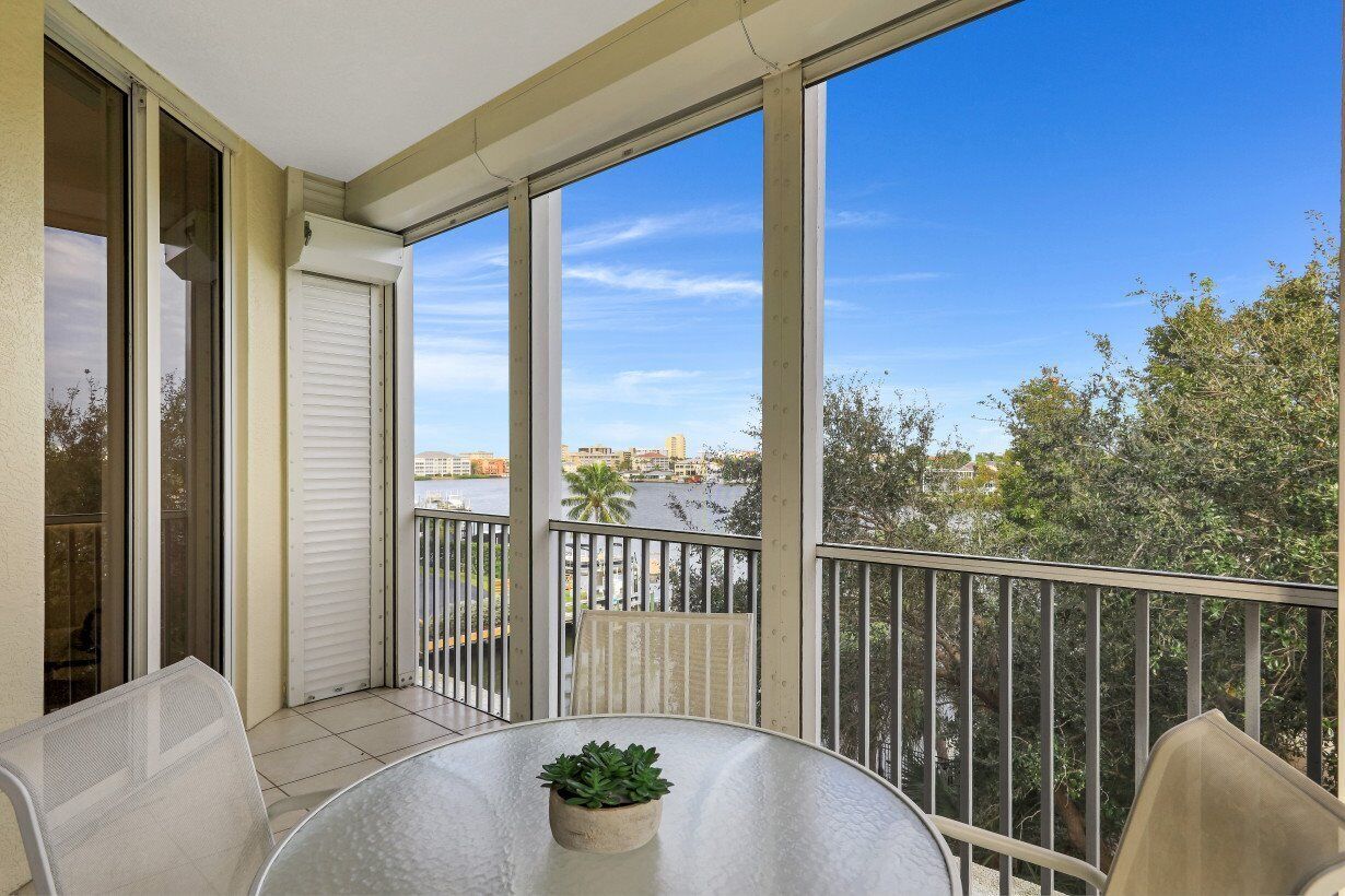 A balcony with a glass table and chairs, overlooking a river and buildings.