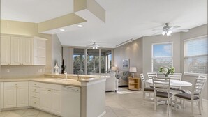 A modern kitchen with white cabinetry, a central island, and a dining area with a round table and chairs. - Regatta - William Raveis Rentals (Naples)