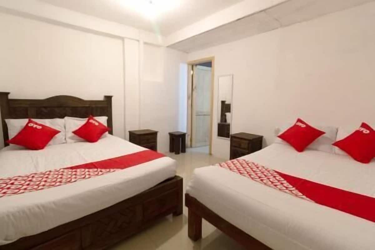 Habitación doble con dos camas, cada una con almohadas rojas y una colcha blanca. Hay dos mesitas de noche y un espejo en la pared.