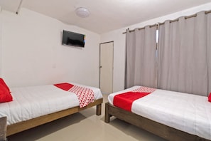 Two single beds with red and white bedding, a television on the wall, a door, and curtains.
