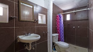 Un baño con lavamanos, espejo, inodoro, cortina de ducha y paredes con baldosas.