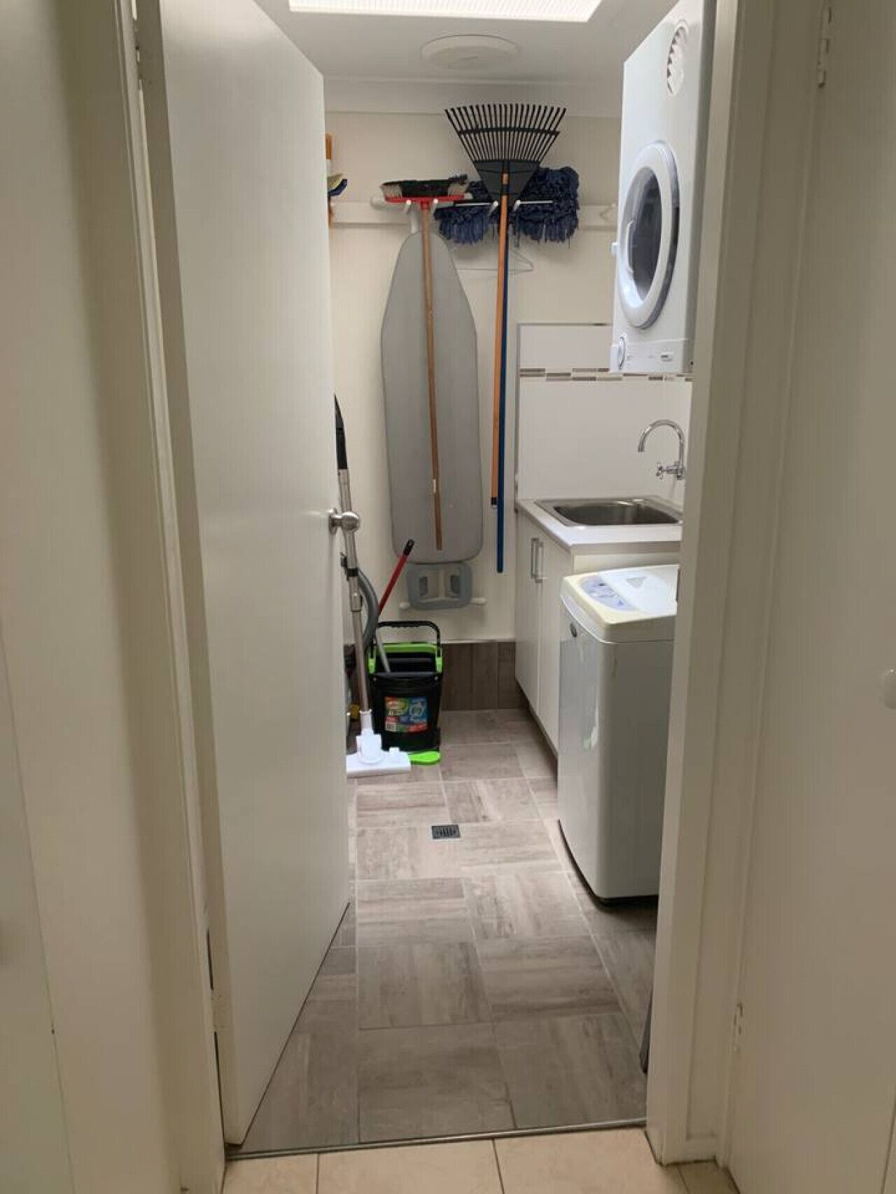 A narrow hallway with a washing machine, a sink, and cleaning supplies.