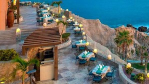 Un espacio de comedor al aire libre con mesas y sillas, con vistas a un paisaje costero.