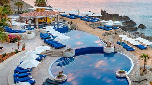 Zona de piscina con sillones de descanso y sombrillas, rodeada por un litoral rocoso.
