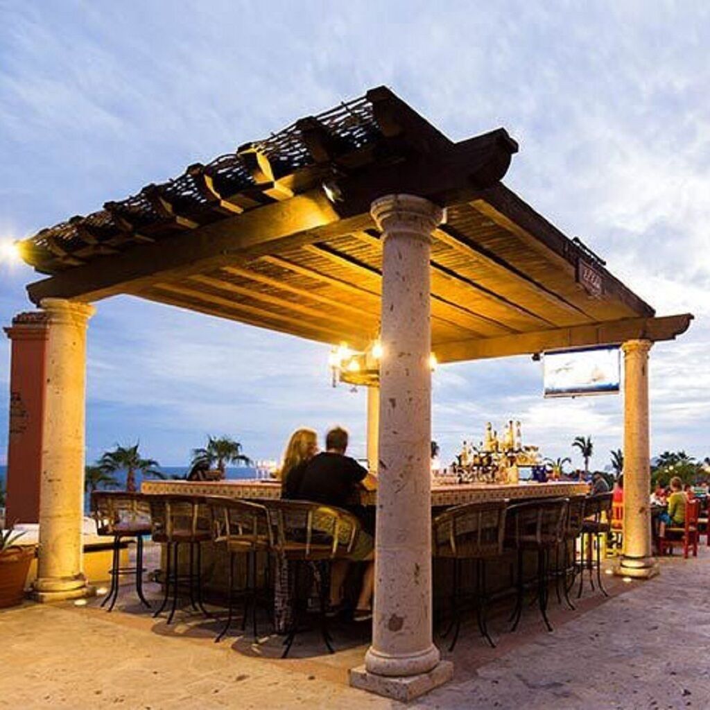 An outdoor dining area with a pergola, tables, and chairs, surrounded by columns.