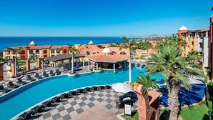 Un resort con una gran piscina, sillones de descanso y vista al océano.
