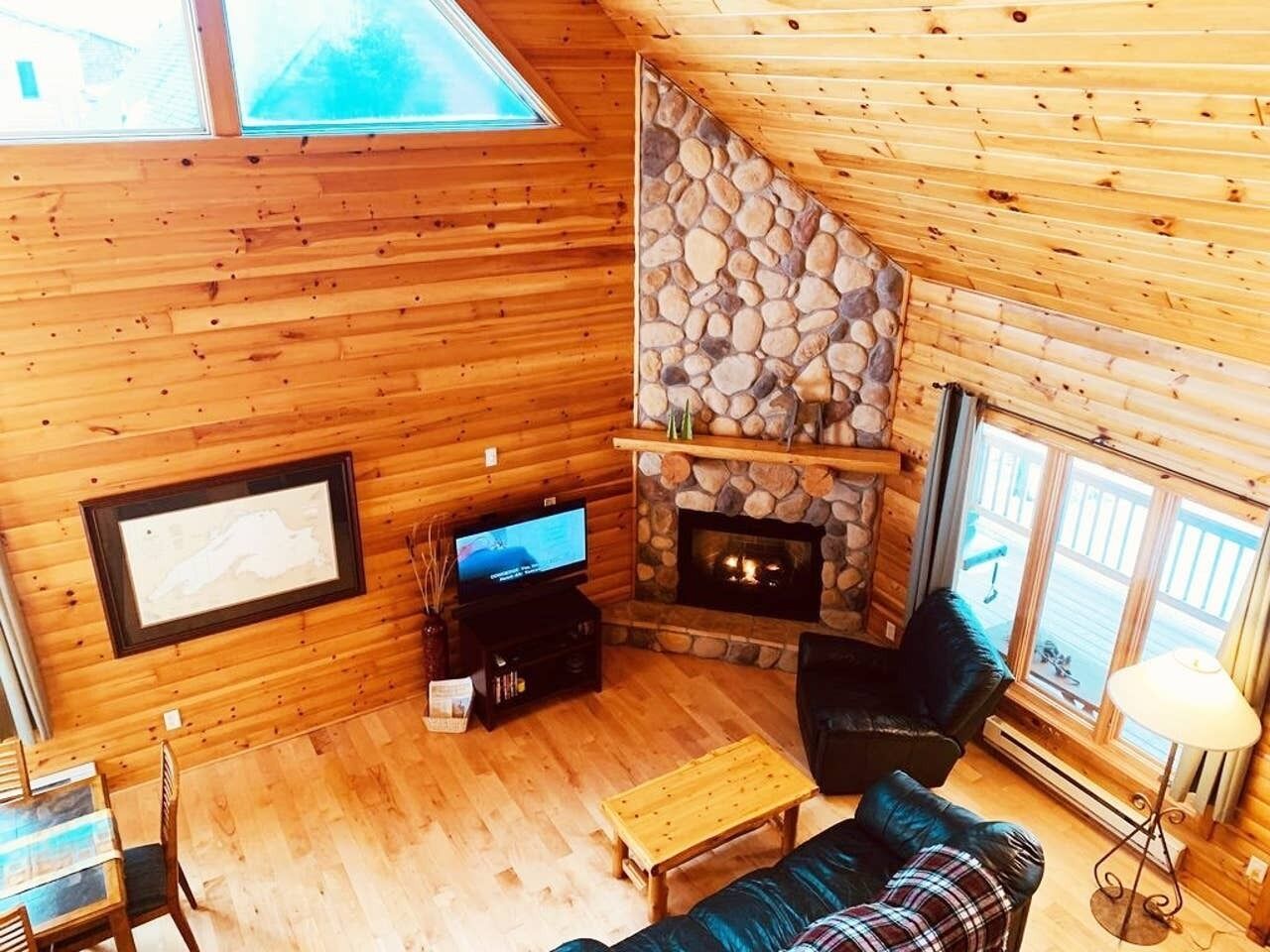 Interior acogedor de una cabaña con chimenea de piedra, paredes de madera, televisor y un espacio de estar cómodo.