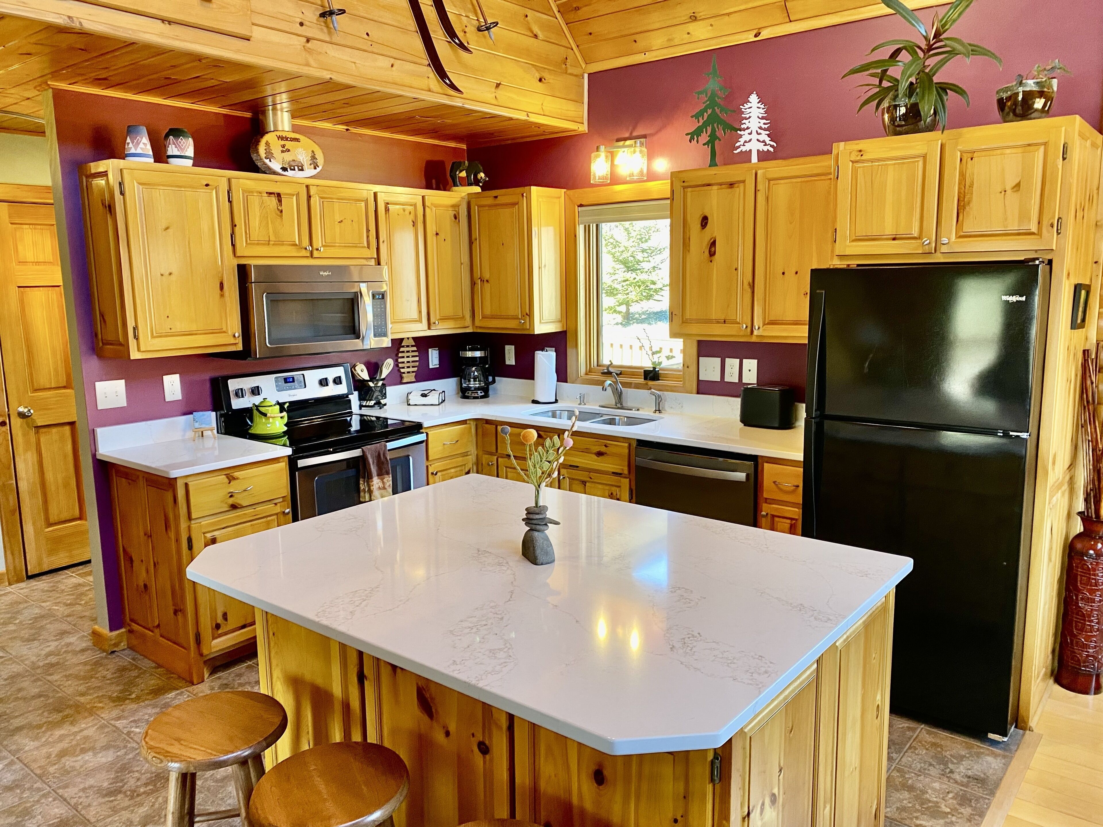 A kitchen with wooden cabinets, a central island, a black refrigerator, and a microwave.