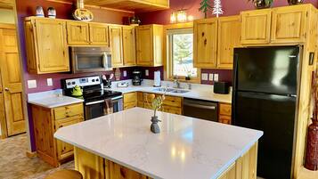 A kitchen with wooden cabinets, a central island, a black refrigerator, and a microwave.