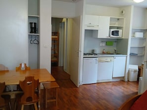 Une cuisine compacte Ă©quipĂ©e dâun four Ă micro-ondes, dâune cuisiniĂšre et dâun lave-vaisselle. On y trouve une table Ă manger avec des chaises et un plancher en bois.
