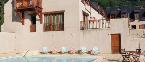 A building with a swimming pool, a balcony, and a view of green hills.