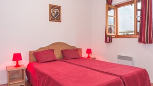 A bedroom with a wooden bed, two red lamps, a window with curtains, and a wall-mounted picture. - Cozy 2-room apartment with terrace and pool in Vignec (Vignec)