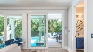 A modern interior with a pool area visible through glass doors, a seating area with a blue sofa, and a kitchen with blue cabinets. - 113 Custom Sandcastle, Pool, Hot Tub, Kids Suite (Hilton Head Island)