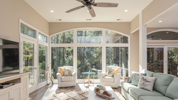 A spacious living room with a large arched window, a ceiling fan, and a television.