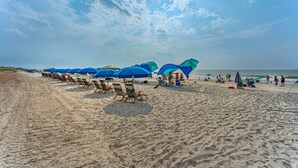 Een strand met rijen blauwe parasols en ligstoelen, een zandstrand en de oceaan op de achtergrond.
