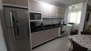 A compact kitchen with stainless steel appliances, a microwave, and a gas stove. There is a dining area with a patterned table and chairs. - 224, Great apartment a few meters from the beach (Bombas)