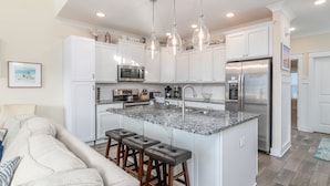 A modern kitchen with white cabinets, a granite island, stainless steel appliances, and pendant lighting. - Luxury Beach Home | Heated Pool | Pets OK (Hilton Head Island)