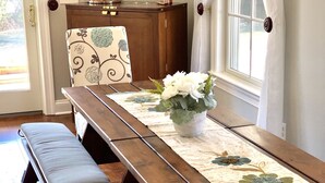 Una mesa de madera con bancos, un camino de mesa floral y un florero con flores.