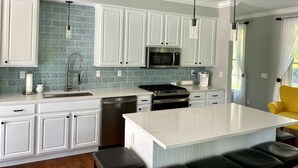 Una cocina moderna con armarios blancos, un microondas de acero inoxidable y una isla grande con taburetes de bar.
