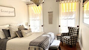 Un dormitorio con una cama, una silla, un banco y un adorno de macramé en la pared.