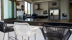 A modern kitchen with a large island, black and white wicker chairs, and a stainless steel refrigerator.