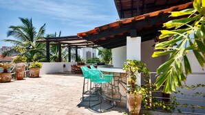 A rooftop patio with outdoor seating, potted plants, and a view of palm trees and buildings.