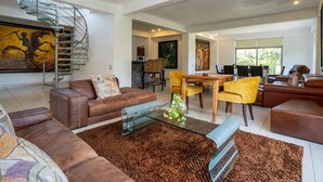 A modern living room with a brown leather sofa, a glass coffee table, and a dining area with yellow chairs.