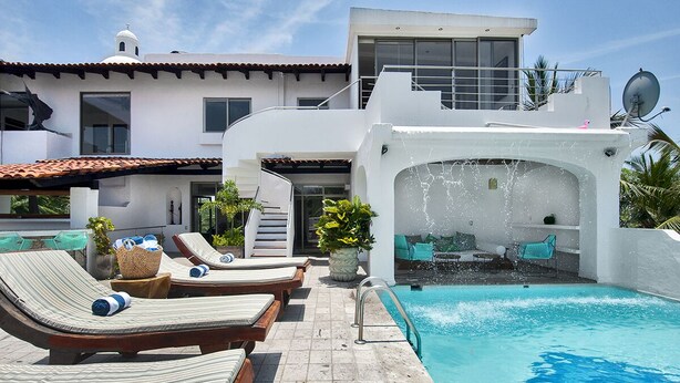 A modern pool area with lounge chairs, a small pool, and a white building with a balcony.