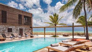 A pool area with lounge chairs, a wooden deck, and a view of the beach. - Silver Sands Villa Turks and Caicos – 8-Bedroom Luxury Beachfront Villa with Gym & Padel Court (Thompson Cove)