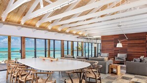 A spacious room with a large round table, multiple chairs, a sofa, and a view of the ocean. - Silver Sands Villa Turks and Caicos – 8-Bedroom Luxury Beachfront Villa with Gym & Padel Court (Thompson Cove)