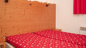 Un dormitorio con cabecera de madera, dos lámparas de noche, una colcha roja con estampado floral, una mesita de noche de madera y una cortina roja.