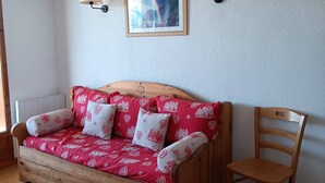 Una cama de madera con ropa de cama estampada en rojo y blanco, dos lámparas de pared y un cuadro en la pared.