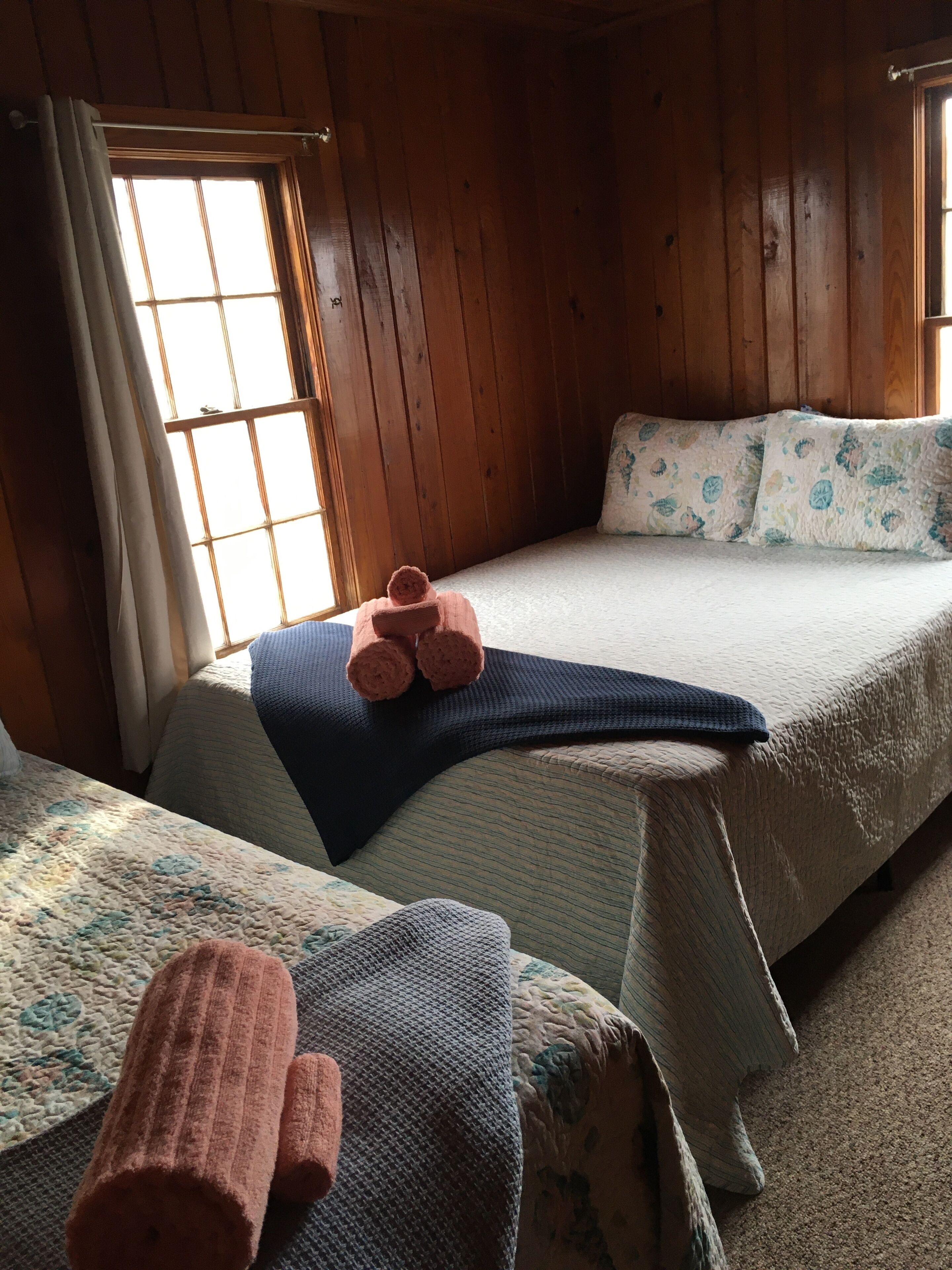 Een kamer in chaletstijl met twee bedden, houten wanden, een raam met gordijnen en een gewatteerde sprei.