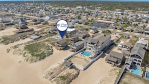 An aerial view of a coastal residential area with houses, a beach, and a large building with a swimming pool.