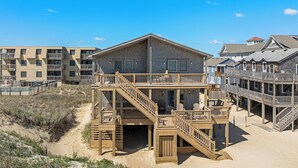 A beachfront property with a wooden deck, multiple balconies, and a sandy beach area.