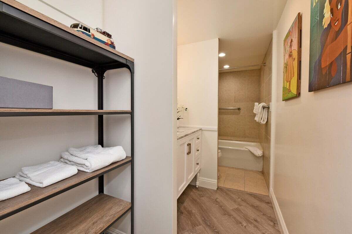A bathroom with a shower, a sink, and a toilet. There is a shelf with folded towels and a small toy car.