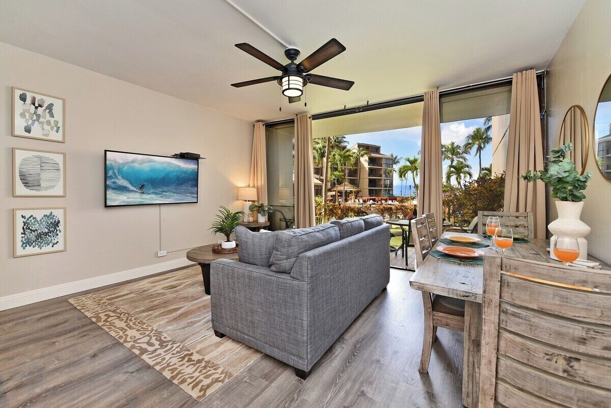 A modern living room with a gray sofa, a ceiling fan, and a large TV.