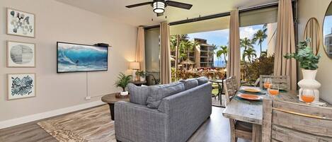 A modern living room with a gray sofa, a ceiling fan, and a large TV.