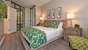 Un dormitorio con cama, mesitas de noche, ventilador de techo y una puerta que da a otra habitación.