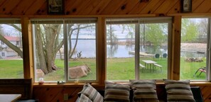Une cabane dotée de grandes fenêtres donnant sur un lac, avec une cour verdoyante et une table de pique-nique.